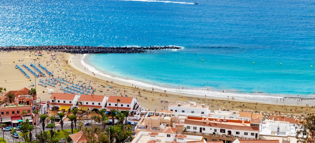 Playa de las Vistas in Los Cristianos, Teneriffa: breiter heller Sandstrand mit Liegen, ruhigem Wasser und Promenade vor dem Ferienort.