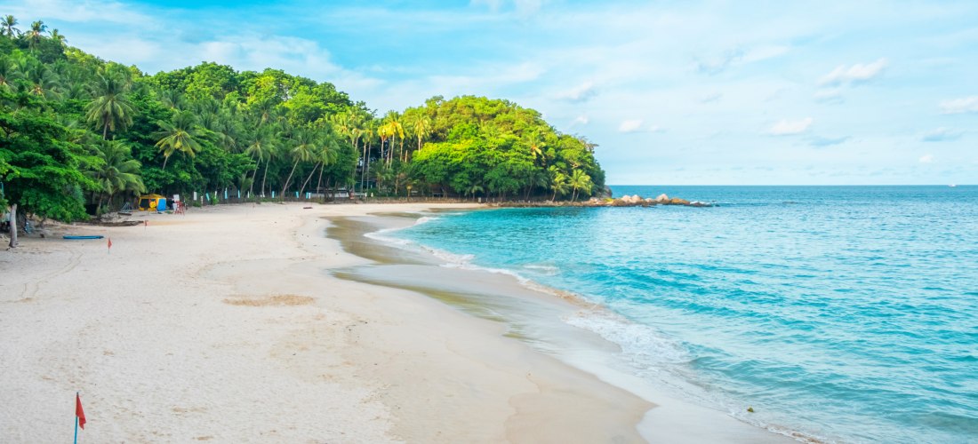 Einsamer Blick auf den idyllischen Freedom Beach in Phuket mit feinem weißen Sand, türkisblauem Meer und üppigem Dschungel im Hintergrund.