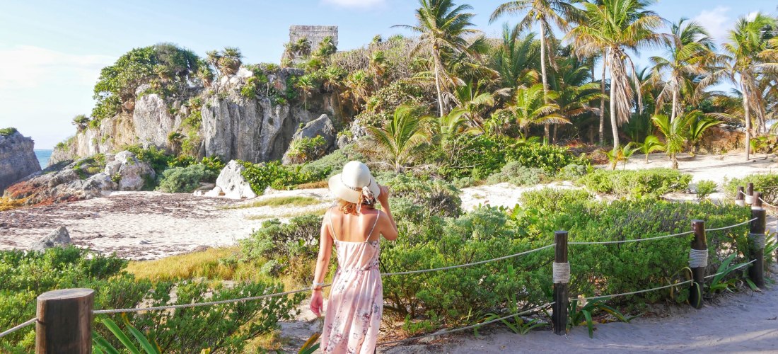 Frau mit Sommerkleid und Hut blickt auf die Tulum Ruinen in Mexiko – Maya-Tempel am Meer, eines der schönsten Reiseziele 2025/2026