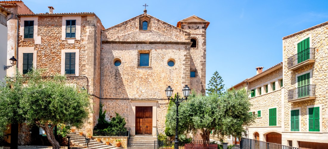 Pfarrkirche Sant Joan Baptista im Dorf Deià auf Mallorca mit typischer Sandsteinfassade und kleinem Platz davor