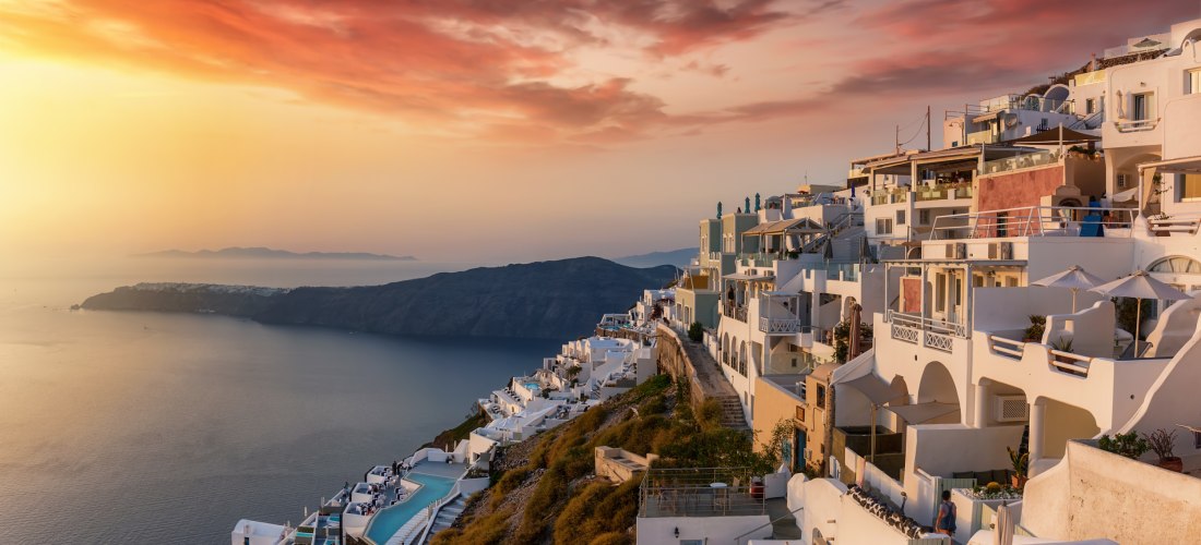 Imerovigli bei Sonnenuntergang: Terrassenhotels mit Infinitypool an der Caldera, goldener Himmel über Thirassia und Oia in der Ferne