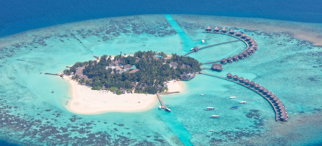 Luftaufnahme einer Malediven-Insel mit weißen Sandstränden, türkisblauem Wasser und Wasserbungalows, die halbkreisförmig ins Meer gebaut sind.
