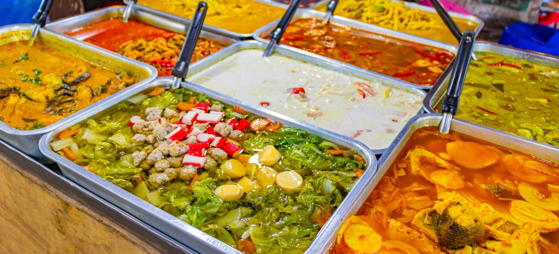 Auswahl an traditionellen thailändischen Currys in leuchtenden Farben, frisch zubereitet auf einem Streetfood-Markt in Koh Samui, Thailand.