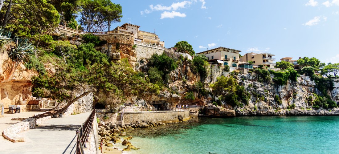 Felsenpromenade an der Cala Marçal auf Mallorca mit türkisfarbenem Wasser und Häusern auf den Klippen