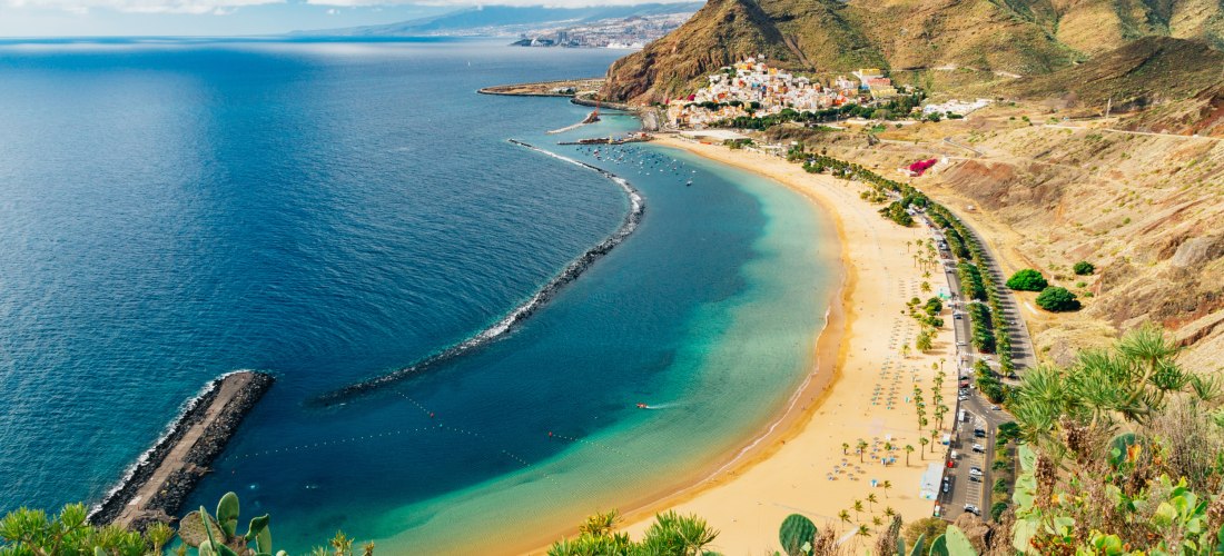 Playa de Las Teresitas nahe San Andrés im Norden Teneriffas: langer heller Sandstrand mit Palmen, ruhigem Wasser durch Wellenbrecher und Blick auf die Berge.