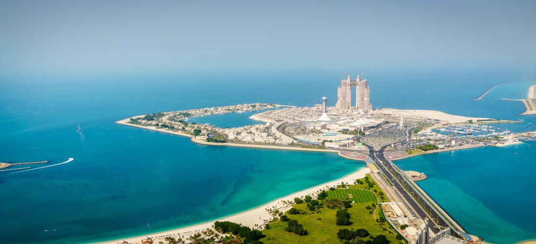 Luftaufnahme der Insel Abu Dhabi mit türkisfarbenem Wasser, modernen Hochhäusern und einer Brücke, die die Insel mit dem Festland verbindet
