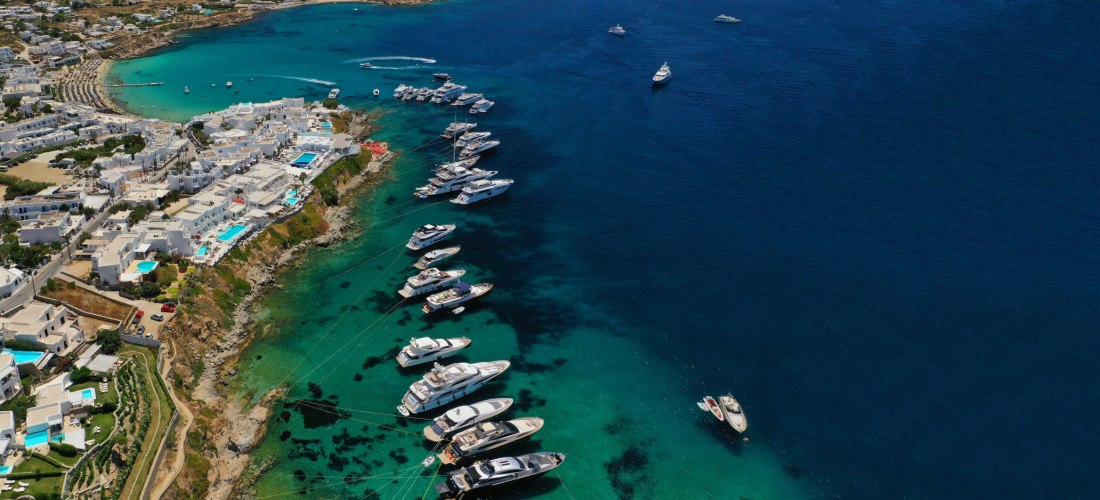uxusyachten vor der Küste von Mykonos, Griechenland, mit türkisfarbenem Wasser und weißen Häusern an der Bucht
