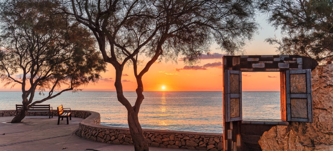 Sonnenuntergang an der Promenade von Cala Millor auf Mallorca mit Blick aufs Meer durch ein kunstvolles Fensterobjekt