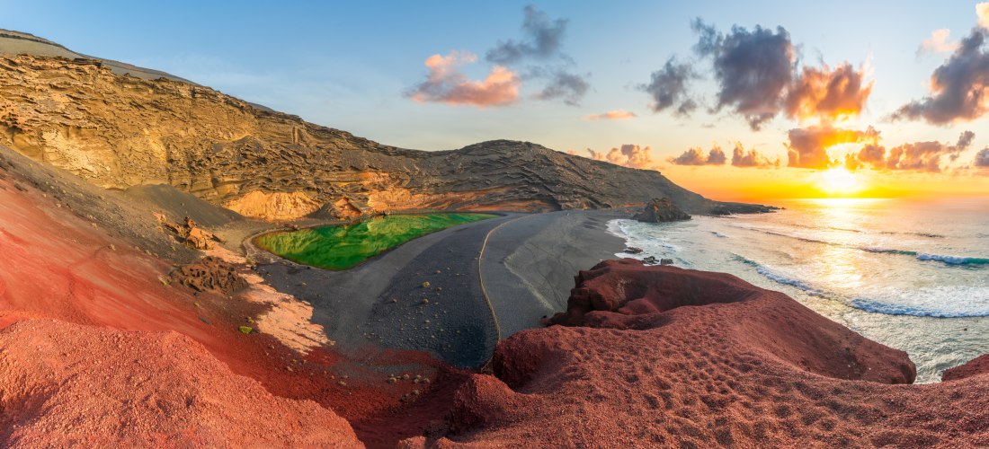 Panoramablick auf den grünen El Golfo Kratersee auf Lanzarote mit schwarzem Strand, rotem Lavagestein und Sonnenuntergang am Atlantik.