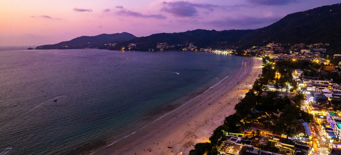 Luftaufnahme vom Patong Beach auf Phuket bei Sonnenuntergang mit bunten Lichtern, Restaurants und Bars – perfektes Ziel für Strandurlaub und Nachtleben 2025/2026