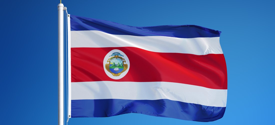 Die Nationalflagge von Costa Rica weht vor einem klaren, blauen Himmel. Die Flagge zeigt horizontale Streifen in Blau, Weiß, Rot, Weiß und Blau mit dem Wappen in der Mitte des roten Streifens
