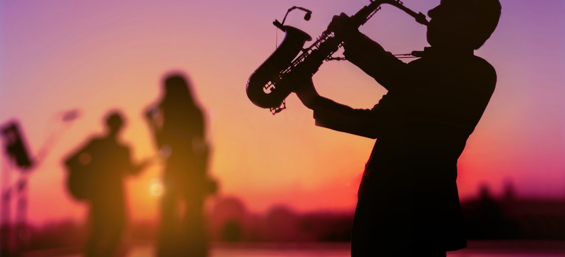 Silhouette eines Saxophonisten in der Dämmerung, der als Triomusiker auftritt. Hintergrund für Festival, verschwommen, Sonnenuntergang