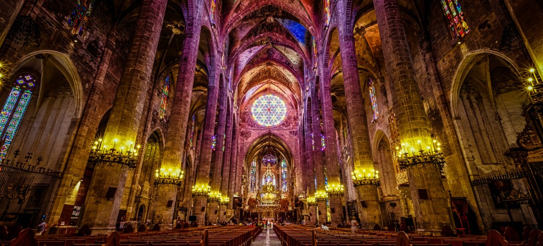 Innenansicht der gotischen Kathedrale La Seu in Palma mit bunten Glasfenstern und leuchtenden Kronleuchtern