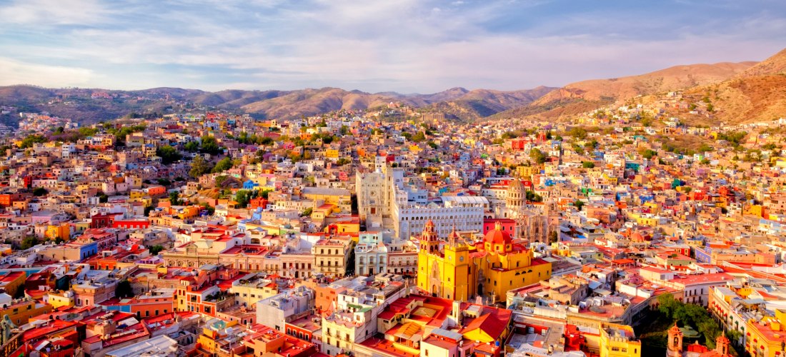 Panoramablick auf die farbenfrohen Häuser und historischen Gebäude von Guanajuato, Mexiko, umgeben von Hügeln unter einem blauen Himmel
