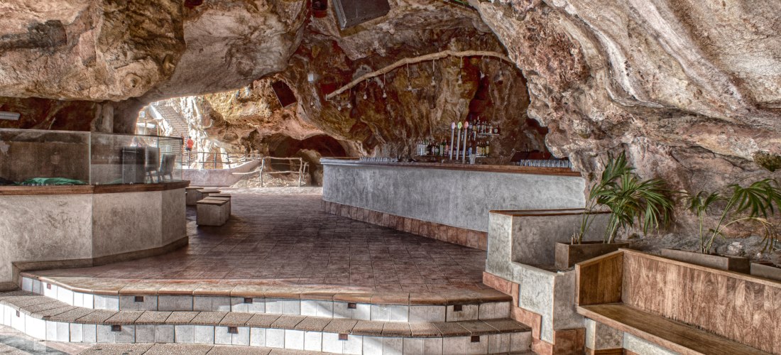 Innenansicht der Cova d'en Xoroi auf Menorca: eine Bar mit Tischen und Theke, eingebettet in die natürlichen Felsen einer großen Höhle.