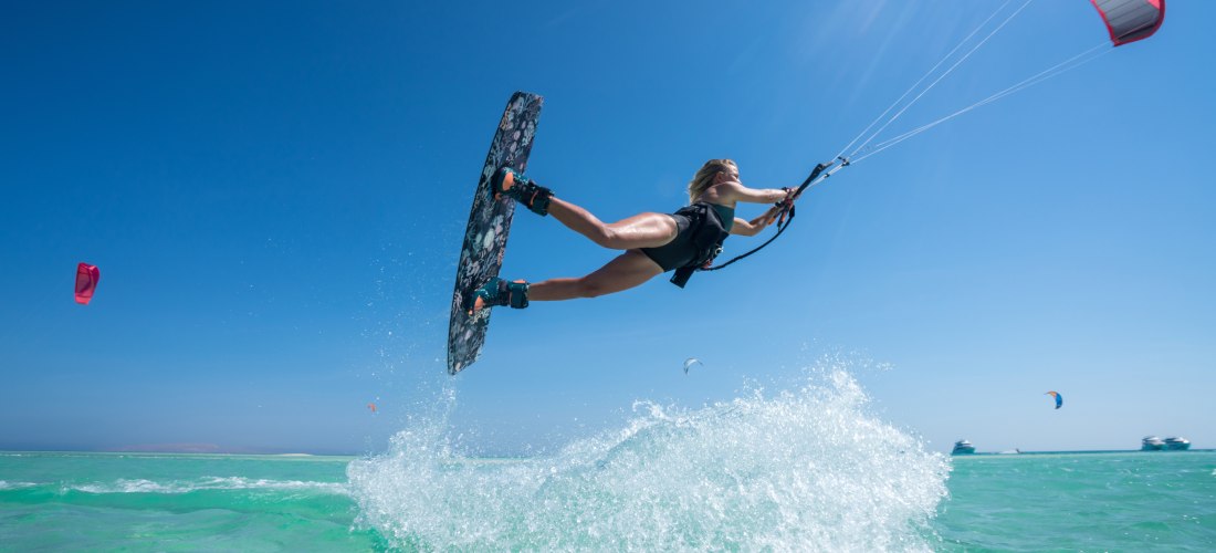 Frau beim Kitesurfen macht einen Sprung über türkisfarbenem Wasser unter strahlend blauem Himmel in der Karibik