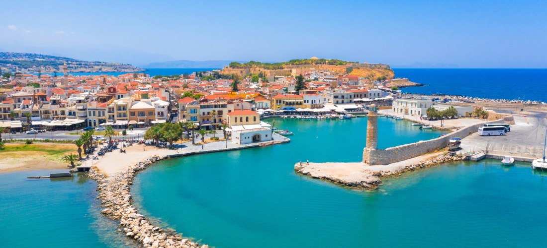 Luftaufnahme des Hafens von Rethymno auf Kreta mit Leuchtturm, türkisblauem Wasser und der historischen Altstadt im Hintergrund