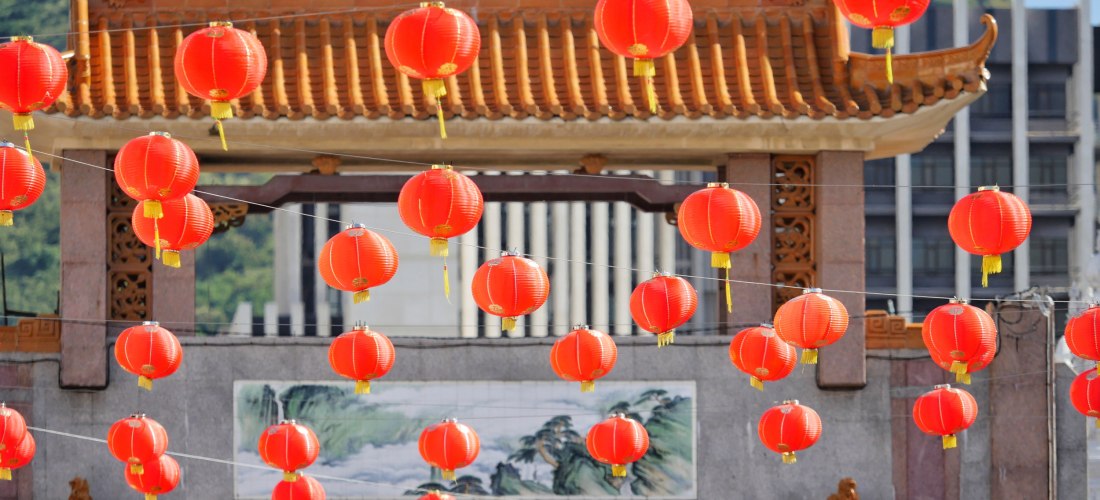 wunderschöne Szene mit einem traditionellen chinesischen Tor, das mit zahlreichen roten Laternen geschmückt ist. Das Tor besitzt ein kunstvoll verziertes, geschwungenes Dach mit Drachenfiguren an den Enden, das an klassische chinesische Architektur erinne
