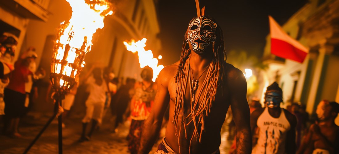 Menschen in traditionellen Masken und mit brennenden Fackeln bei einem nächtlichen Feuerfest