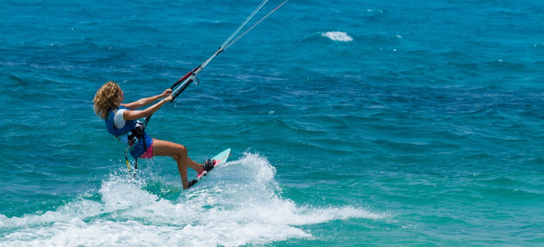 Frau beim Kitesurfen auf türkisblauem Wasser, zieht mit ihrem Kite über die Wellen