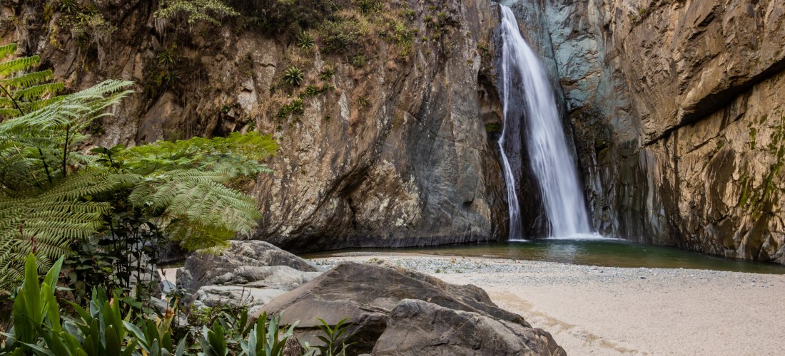Beeindruckender Wasserfall inmitten einer Felsenschlucht in der Dominikanischen Republik, umgeben von üppiger Vegetation und Felsen