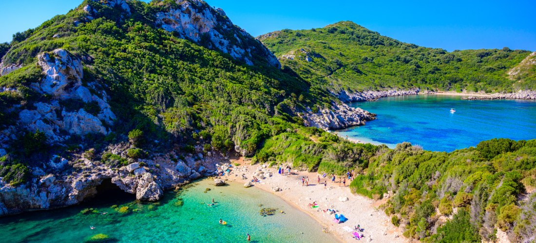 Naturidylle auf Korfu: Die bekannte Zwillingsbucht Porto Timoni zeigt sich hier von oben – zwei geschützte Badebuchten mit kristallklarem Wasser, umgeben von dicht bewachsenen Hügeln und Felswänden. Ein Paradies für Ruhesuchende, Naturliebhaber und Schnor