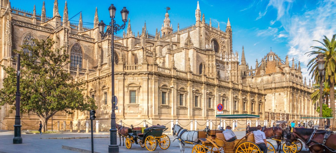 Kathedrale von Sevilla an einem sonnigen Tag mit Pferdekutschen im Vordergrund, imposante gotische Architektur mit vielen Türmchen und Verzierungen.