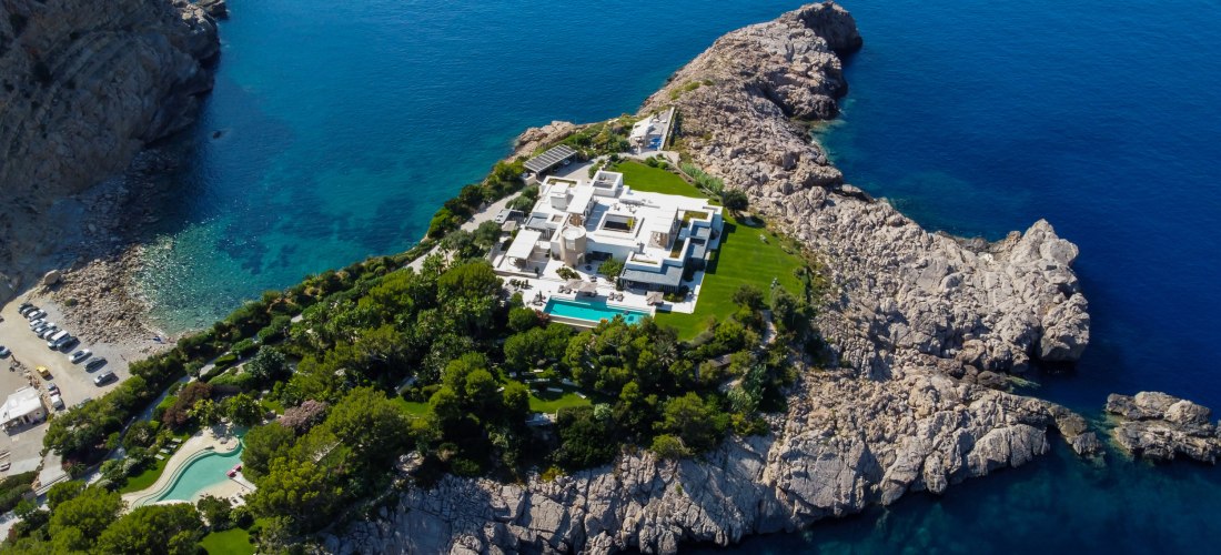 Eine luxuriöse weiße Villa mit Pool thront auf einer felsigen Landzunge, umgeben von sattgrüner Landschaft und dem tiefblauen Meer. Die moderne Architektur hebt sich von der Natur ab, während das Anwesen absolute Privatsphäre und traumhafte Ausblicke auf 