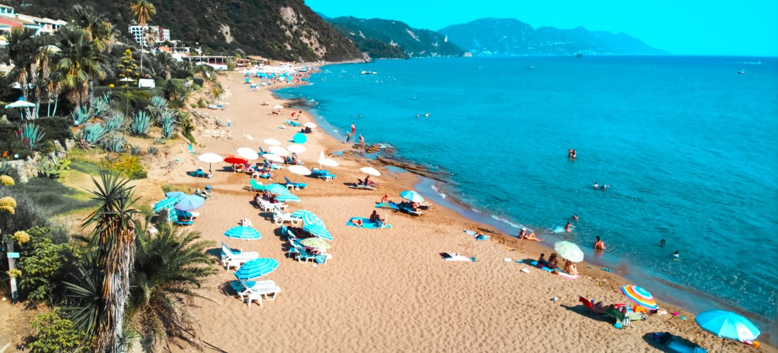Glyfada Beach auf Korfu mit bunten Sonnenschirmen, goldenem Sandstrand und türkisblauem Meer