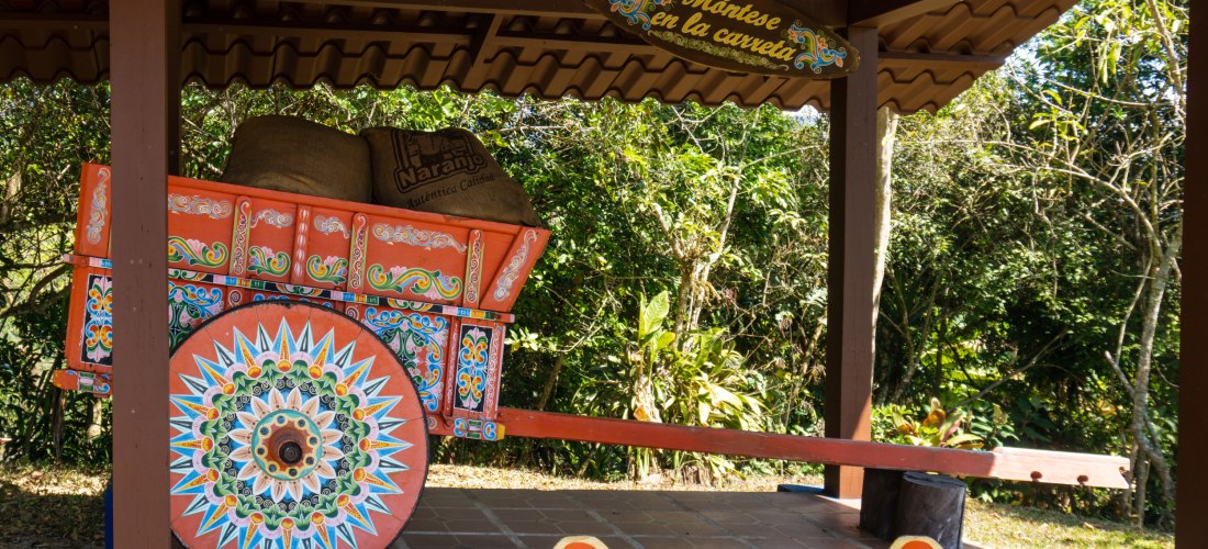 Traditionell bemalter Ochsenkarren aus Costa Rica unter einem Unterstand mit Kaffeesäcken und dekorativem Schild im Hintergrund