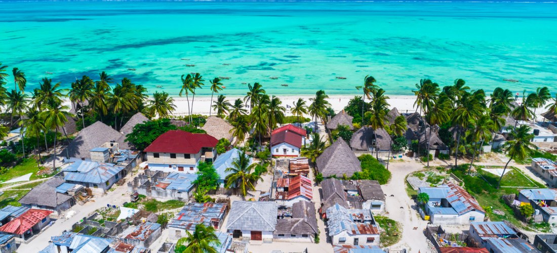 Blick auf ein traditionelles Dorf auf Sansibar mit Palmen, Häusern und Hütten direkt am weißen Sandstrand mit türkisblauem Meer