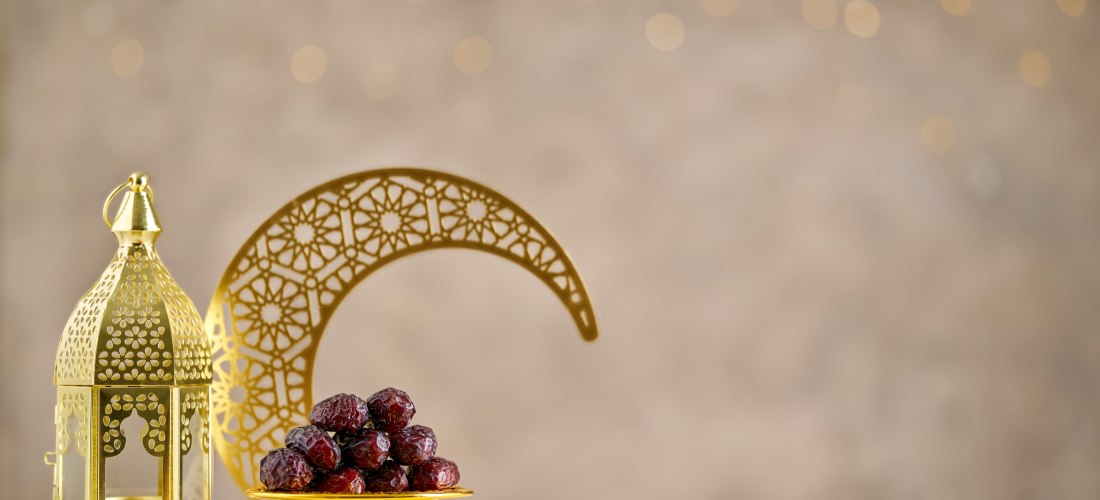 Dieses Bild zeigt eine elegante Ramadan-Dekoration mit klassischen Symbolen. Die goldene Laterne mit orientalischen Mustern erinnert an die spirituelle Bedeutung des Fastenmonats. Datteln, die traditionell zum Fastenbrechen (Iftar) gegessen werden, sind k