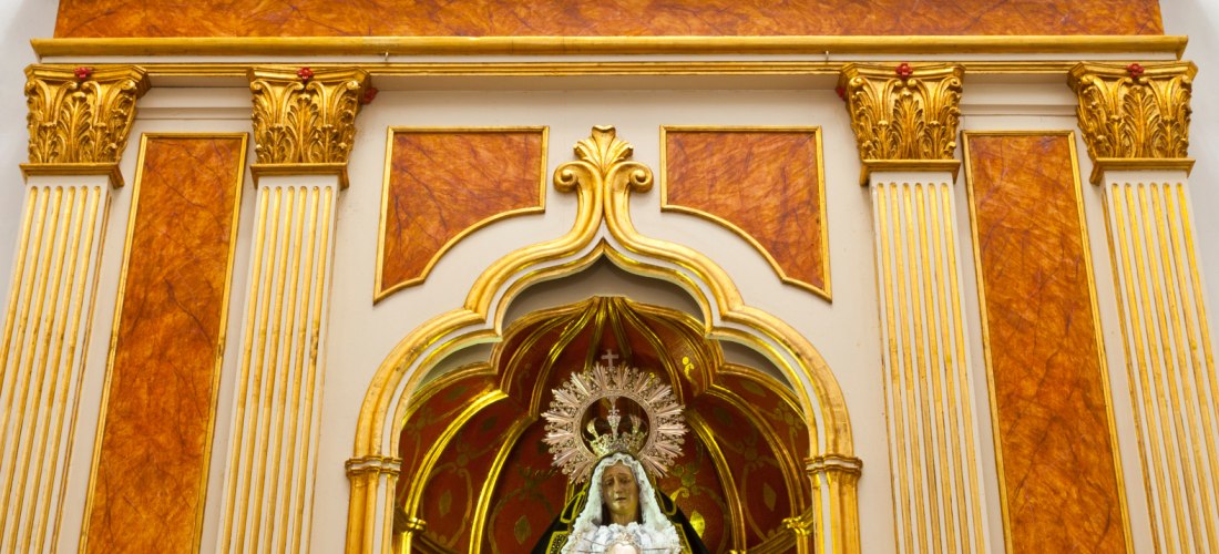 Vergoldeter Altar mit einer Statue der Jungfrau Maria in schwarzem, reich besticktem Gewand. Über der Nische befindet sich ein Symbol mit zwei Herzen, einem Kreuz und Engelsköpfen.