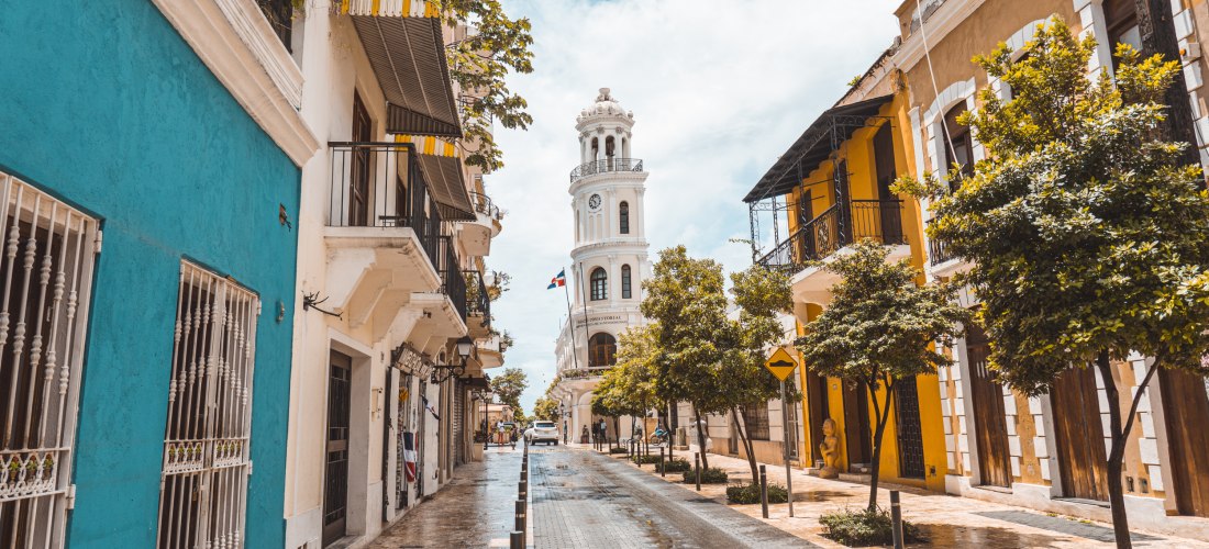 Koloniale Altstadtstraße in Santo Domingo mit bunten Häusern und Blick auf einen weißen Uhrturm, Dominikanische Republik
