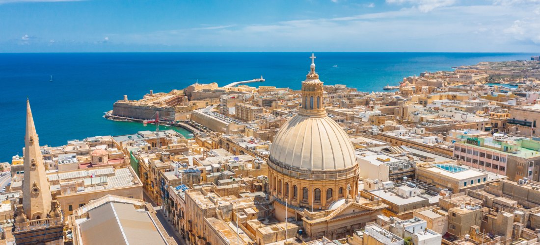 Luftaufnahme von Valletta auf Malta mit der markanten Kuppel der Karmeliterkirche, dem Mittelmeer und dem Grand Harbour im Hintergrund