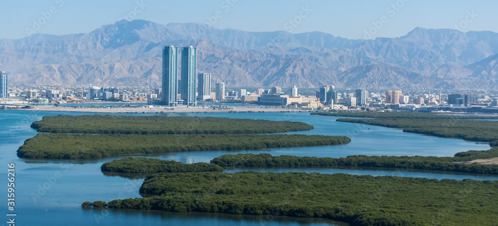 Luftaufnahme einer Stadt mit Hochhäusern, Mangroveninseln und Bergen im Hintergrund