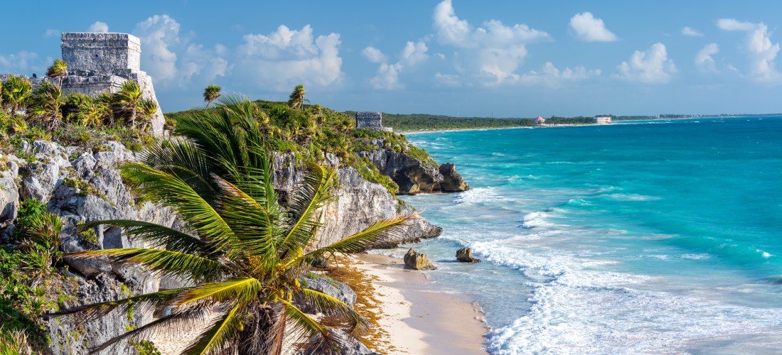 Küstenlandschaft von Tulum, Mexiko, mit Maya-Ruinen auf einer Klippe, türkisblauem Meer, weißem Sandstrand und üppigen Palmen