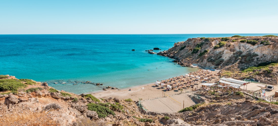 Strandbucht mit Sonnenschirmen und türkisblauem Wasser auf Kreta, umgeben von Felsen