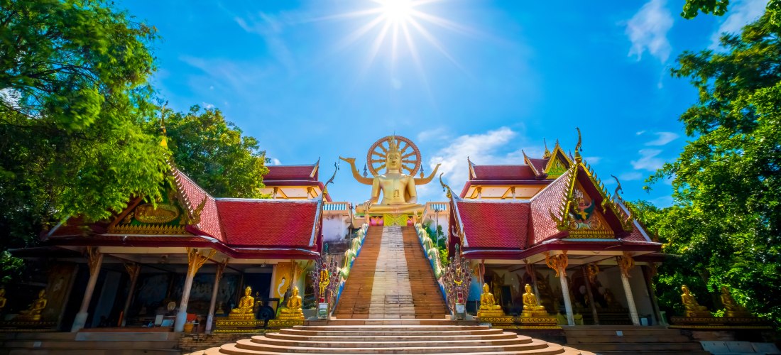 Treppenaufgang zum Wat Phra Yai Tempel auf Koh Samui, Thailand, mit goldener Buddha-Statue und traditioneller Architektur unter strahlender Sonne.