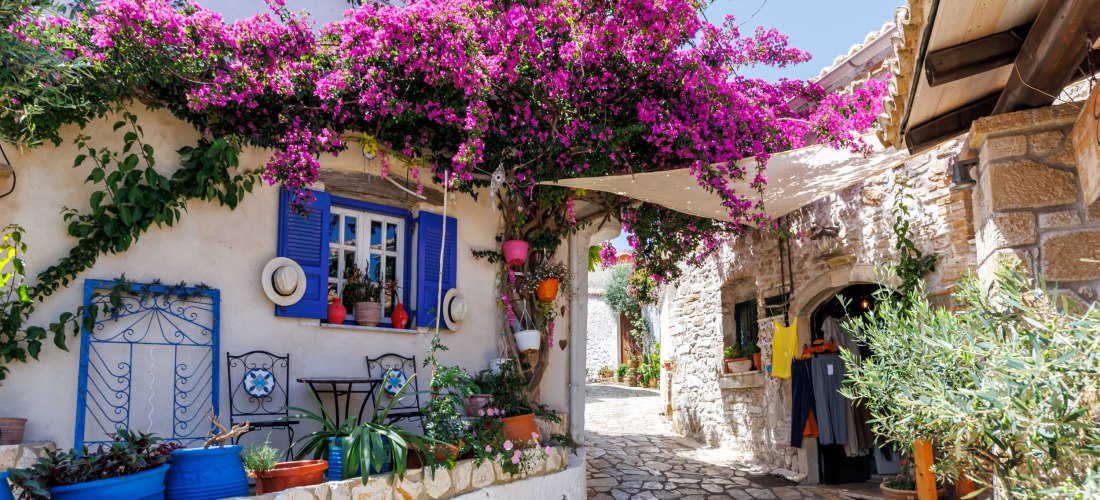 Idyllisches weißes Haus mit blauen Fensterläden und blühender Bougainvillea in einer engen Gasse auf einer griechischen Insel