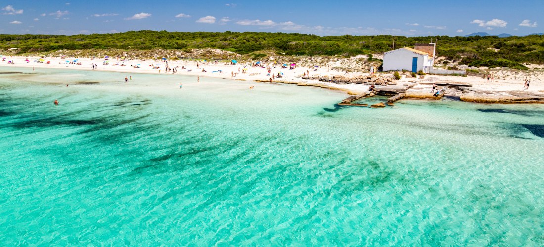 Menschen genießen den weißen Sandstrand und das kristallklare Wasser an einem sonnigen Tag auf Mallorca