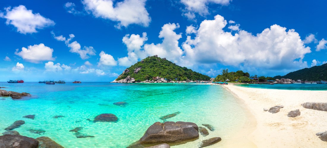  Das Bild zeigt eine spektakuläre tropische Landschaft mit einer schmalen Sandbank, die zwei kleine Inseln miteinander verbindet. Das Wasser rundherum ist kristallklar und in verschiedenen Türkistönen leuchtend. Auf der einen Seite der Sandbank befinden s