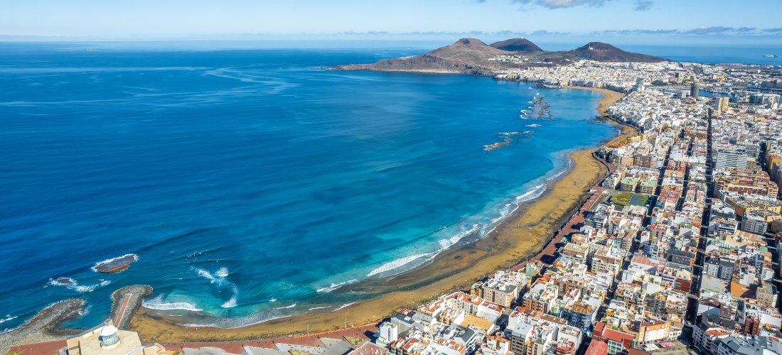 Luftaufnahme von Las Palmas de Gran Canaria mit der langen Playa de Las Canteras, türkisblauem Meer und dichter Bebauung entlang der Küste.