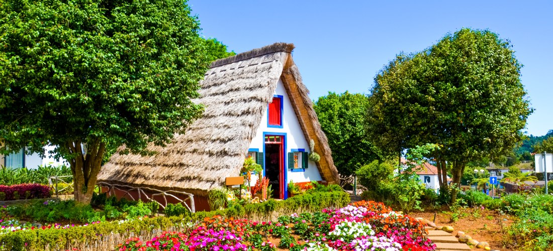 Santana Madeira – Traditionelles Strohdachhaus im Blumenmeer Typisches Strohdachhaus in Santana auf Madeira mit buntem Blumengarten und blauem Himmel
