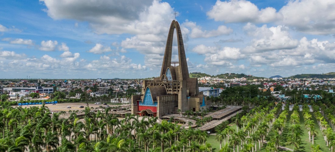 Luftaufnahme der monumentalen Basilika Unserer Lieben Frau von Altagracia in Higüey, umgeben von hohen Palmen, mit Blick auf die Stadt unter einem bewölkten Himmel