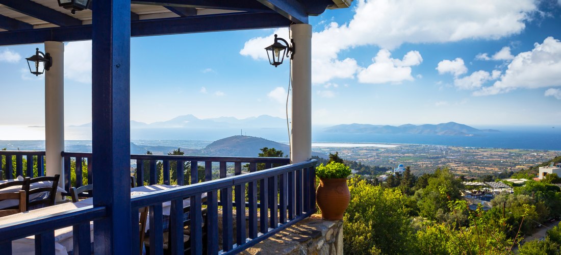 Terrasse einer Taverne im Dorf Zia auf Kos mit blau-weißer Einrichtung und weitem Blick über die Insel bis zum Meer.