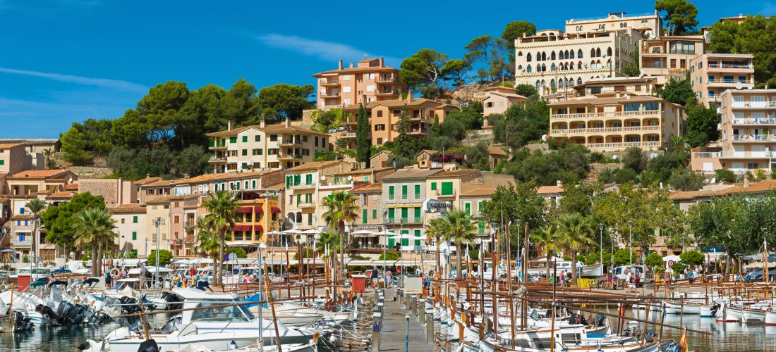Hafen von Port de Sóller auf Mallorca mit traditionellen Booten, bunten Häusern und grünen Hügeln im Hintergrund