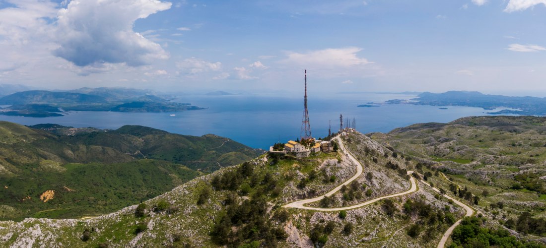 Blick vom Berg Pantokrator auf Korfu: kurvenreiche Straße, Funkmasten und Panoramablick auf das Meer und Nachbarinseln.