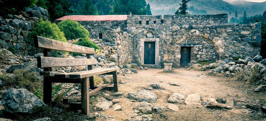 Ruinen der byzantinischen Festung Paleo Pyli auf Kos mit steinernen Mauern, Türen und einer Holzbank im Vordergrund.
