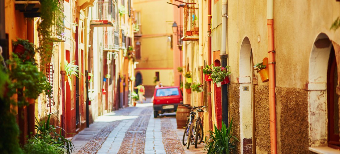 Bunte Altstadtgasse in Bosa auf Sardinien mit Kopfsteinpflaster, Blumen und warmen Fassadenfarben – authentisches Sardinien-Flair an der Westküste